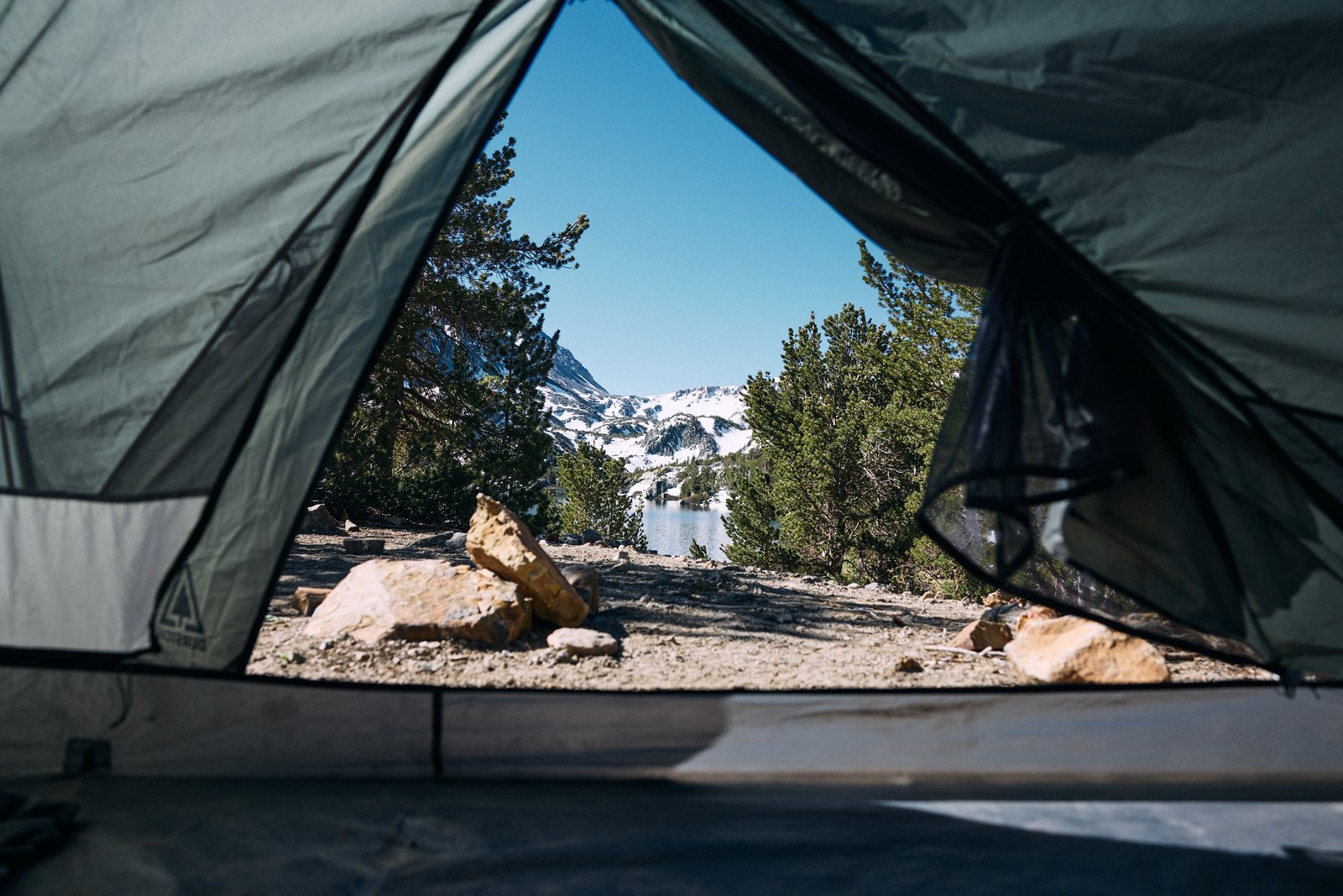 View from tent overlooking alpine lake and snow-capped Sierra peaks
